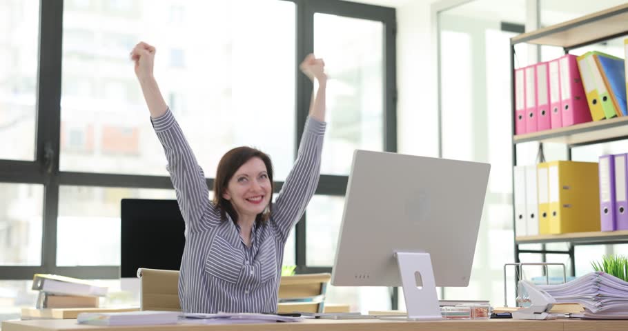 Joyful businesswoman celebrating success at workplace. Manager communicating on smartphone celebrating success
