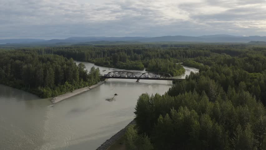 Train traveling over tressel bridge above Susitna River with mountain landscape near Talkeetna, Alaska - 4K Drone
