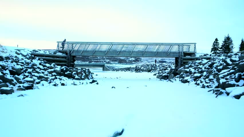 A man running on the frozen river bridge in winter of Hengifoss waterfall in the cold winter of Iceland