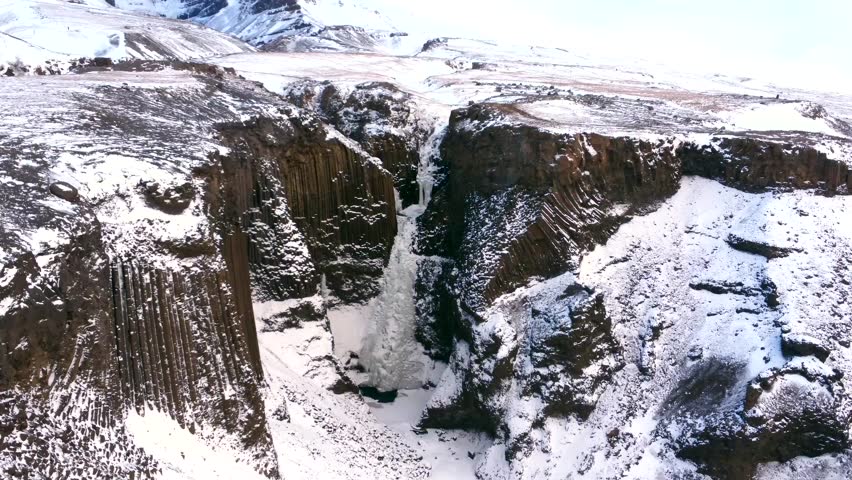 Sunrise at frozen Hengifoss waterfall in the cold Icelandic winter, volcanic cliffs