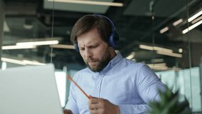 Happy office worker dances and has fun at his desk while wearing headphones and listening to music. A man is playing imaginary drums, holding pencils in his hands as if he is playing the drums. - Powered by Shutterstock - Get 15% off with code: PIKWIZARD15