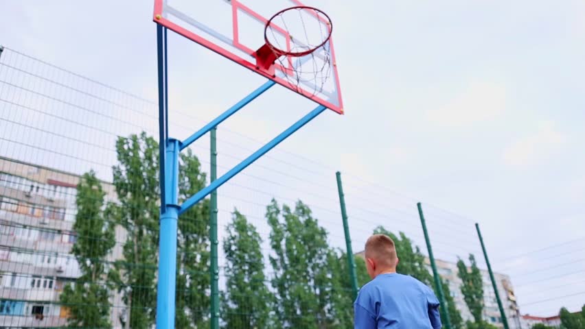 Boy kid dressed in sports uniform playing basketball alone on street city sports playground