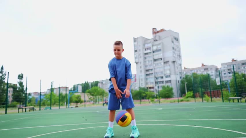 Boy kid dressed in sports uniform playing basketball alone on street city sports playground