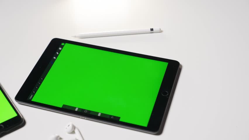 Chroma key.Greenscreen on smartphone and smart tablet earpods and smart pen on white table.High quality moving camera footage