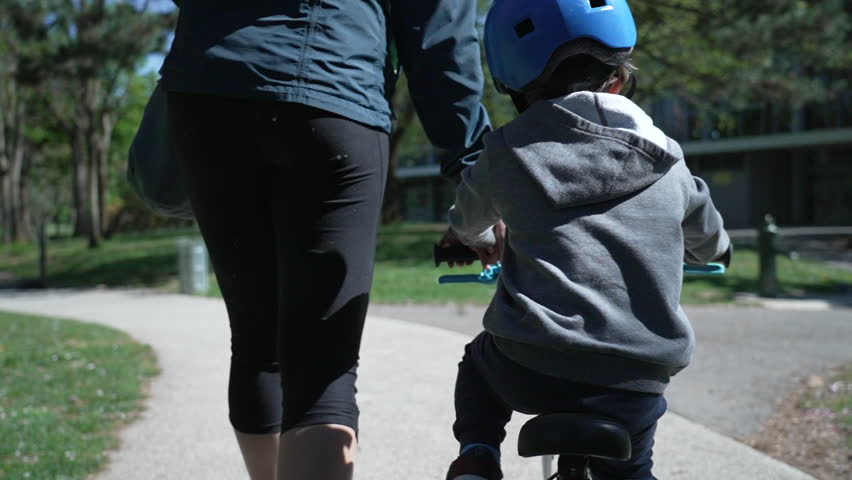 Young boy riding a bike with a blue helmet, guided by an adult in the park. The child is learning to ride, concentrating on balancing and enjoying the outdoor activity