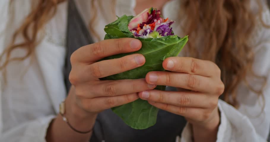 Close-up 4K video of woman eating raw green wrap with leaves of kale shows healthy vegan meal for lunch table. "Food is medicine" concept.