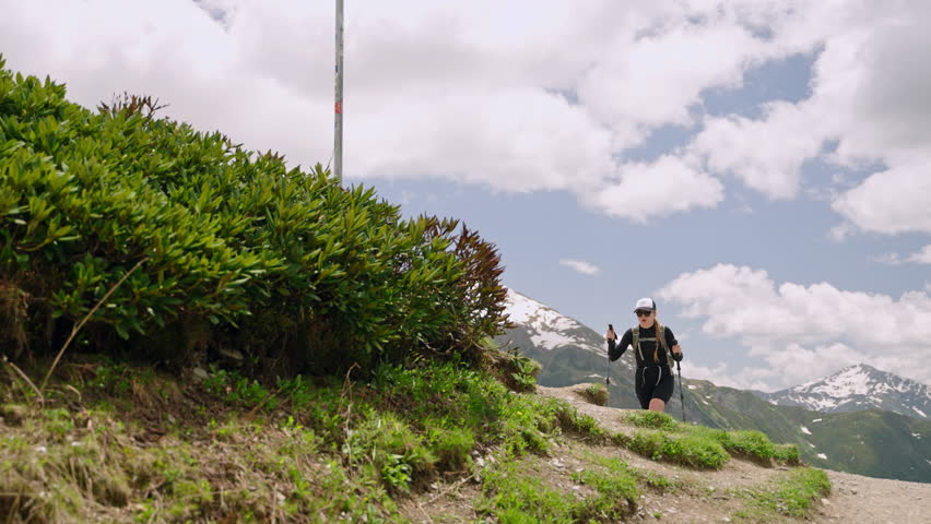 Woman hiking in Svaneti mountains, Georgia. Backpack, trekking poles, active lifestyle. Scenic nature, green hills, snow-capped peaks. Outdoor adventure, explore wilderness, mountain trek. Slowmo