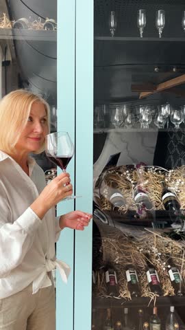 A sophisticated woman, radiating joy and elegance, is relishing a glass of exquisite red wine in a chic kitchen