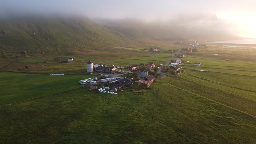 Farm buildings and fields under early morning mist and fog in Lofoten, Northern Norway by the Ryten mountain