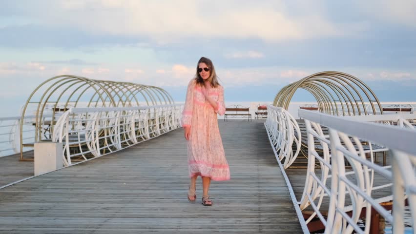 Young woman dynamically dancing on the pier overlooking the lake on a summer day enjoying her vacation on a trip. Wild shot.
