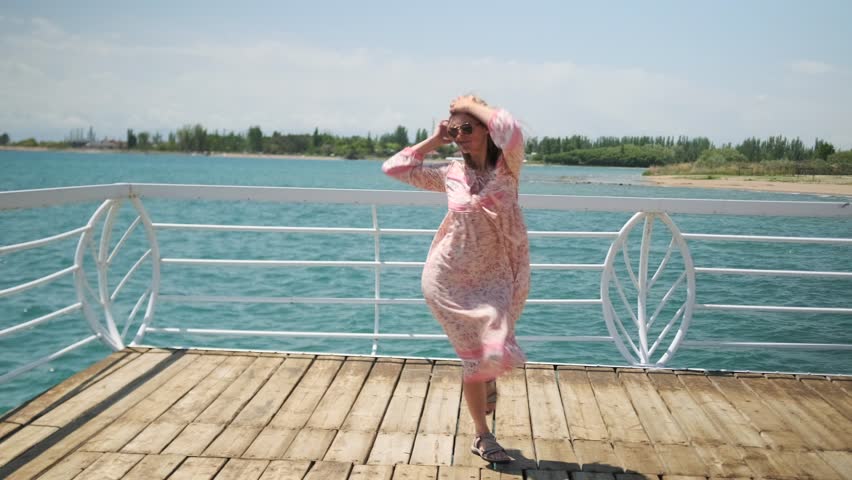 Young Generation Z woman dancing on a wooden pier enjoying freedom and fresh wind on a summer day on vacation by the lake.