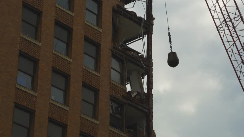 A close-up of the demolition process of an ornate high-rise building in Youngstown, Ohio. The top floors with decorative elements are being dismantled by a crane with a wrecking ball.