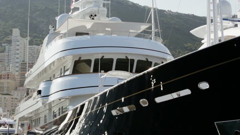 Close up view of Super Yachts moored in Port Hercules, Monaco.  Camera passes ahead of bow of two yachts.