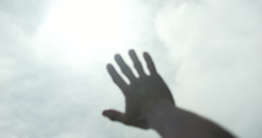 Man in white shirt raising his hand reaching for the sky. The surroundings are calm, with a cloudy sky, creating a tranquil atmosphere. The scene captures a moment of religious contemplation, praying.