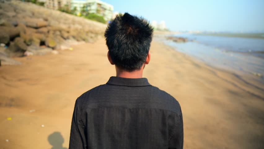 Young Man Walking Beach Back view, Person walks at seascape alone, Mumbai seaside, The sandy shore with rocks, Sea water in background, Men leisure Serene coastal atmosphere, Guy Isolated, Indian,