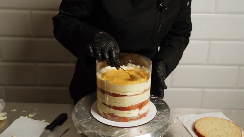 A woman pastry chef is preparing a mango passion fruit cake.The pastry chef applies cream to the cake.The pastry chef collects the layers of the cake.