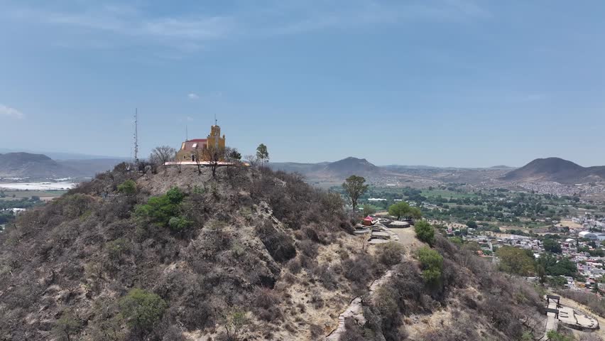 Ascending drone aerial of San Miguel Hill Chapel in Atlixco, Puebla reveals valley cityscape and mountain range on horizon