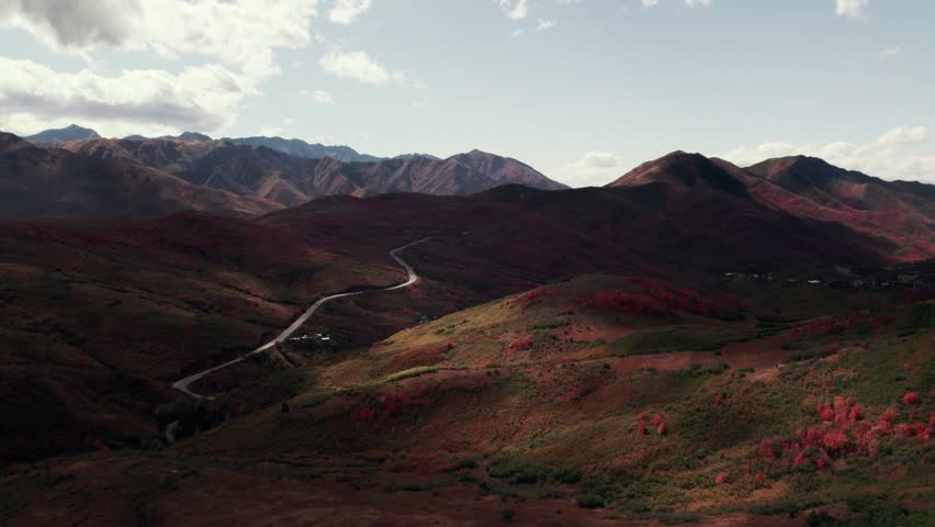 Moody aerial drone shot of Salt Lake City mountain range with fall-colored leaves at 60fps.