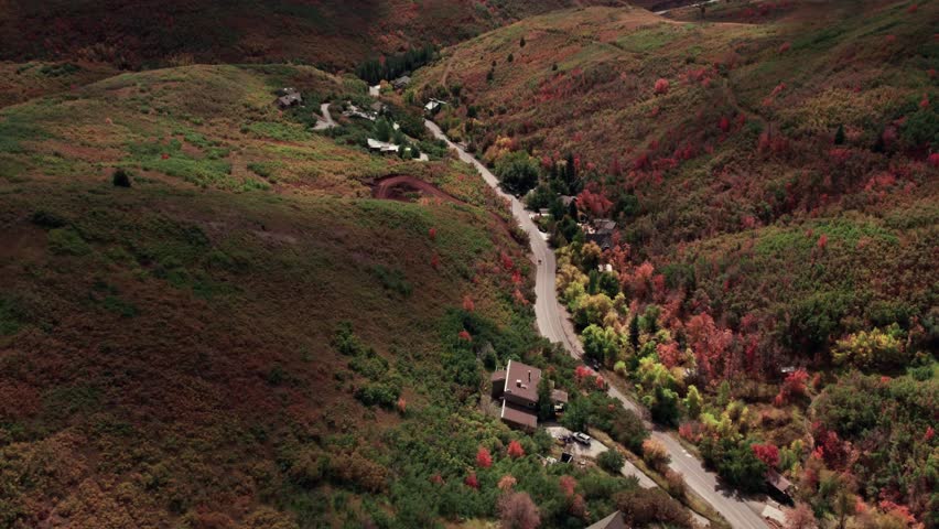 Aerial drone shot of roads winding through the mountain range in Salt Lake City with fall-colored leaves at 60fps.