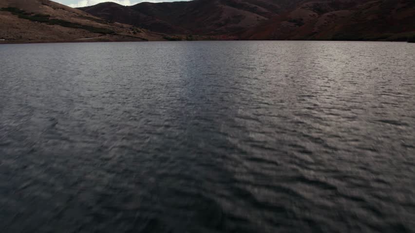 Aerial drone shot flying over the lake and rising to show a mountain range in Salt Lake City with fall-colored leaves at 60fps.