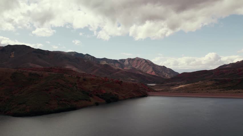 Low-flying aerial drone shot of a lake and mountain ranges in Salt Lake City with fall-colored leaves at 60fps.