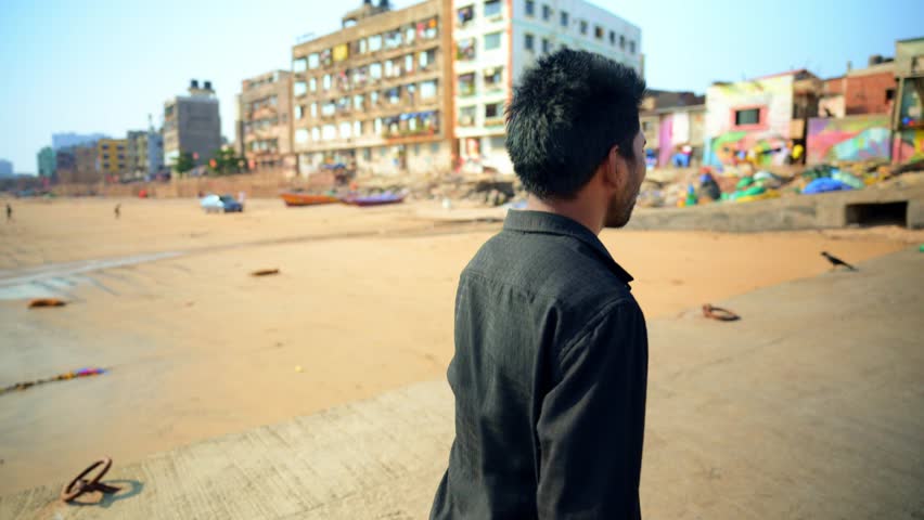 Person Walk And Talk on Sea Shore, Man Walking Alone at the Beach, Looking towards a urban area, With buildings in background, Mix of city and natural elements, with boats, is slow foot it, Indian