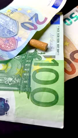 Video of a cigarette stub on a backdrop of Euro notes, portraying the ongoing expense of smoking amidst increasing tobacco prices and taxation.