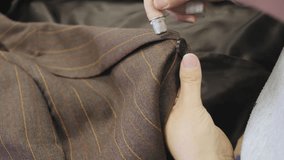 Closeup of sewing a button onto a brown jacket tailored suit in the atelier room - Powered by Shutterstock - Get 15% off with code: PIKWIZARD15
