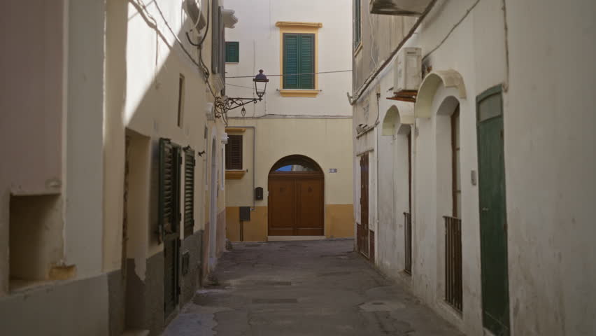 A young woman in a white dress walks through the picturesque narrow streets of gallipoli in puglia, italy, emphasizing the rustic architecture and european charm of the historic area.