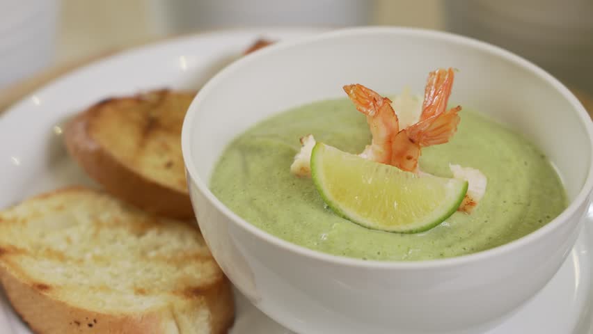 Serving broccoli cream soup with shrimps and toasts