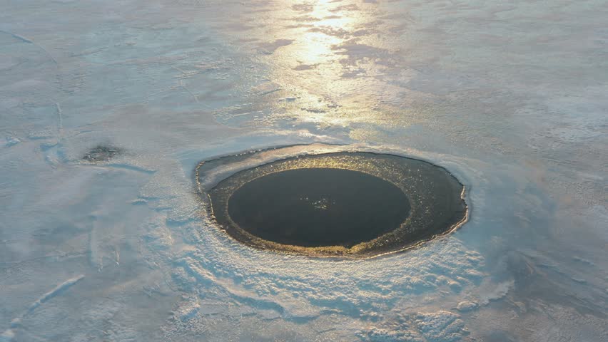 Tilt-Up Drone Shot of Bubbling Ice Hole Revealing Sunset Over Lake