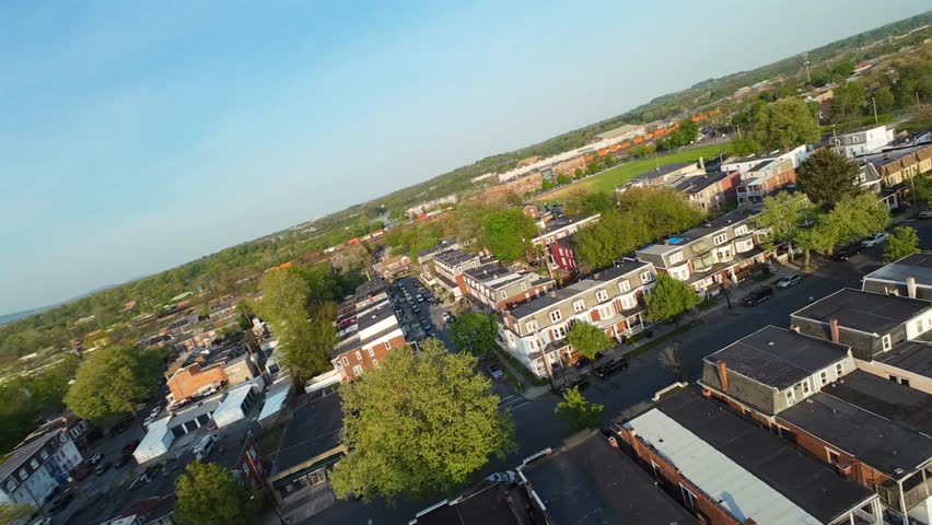 Row of houses in american city during golden sunset. Suburb district with parking cars. Drone fpv flight over street. American town in PA, USA.