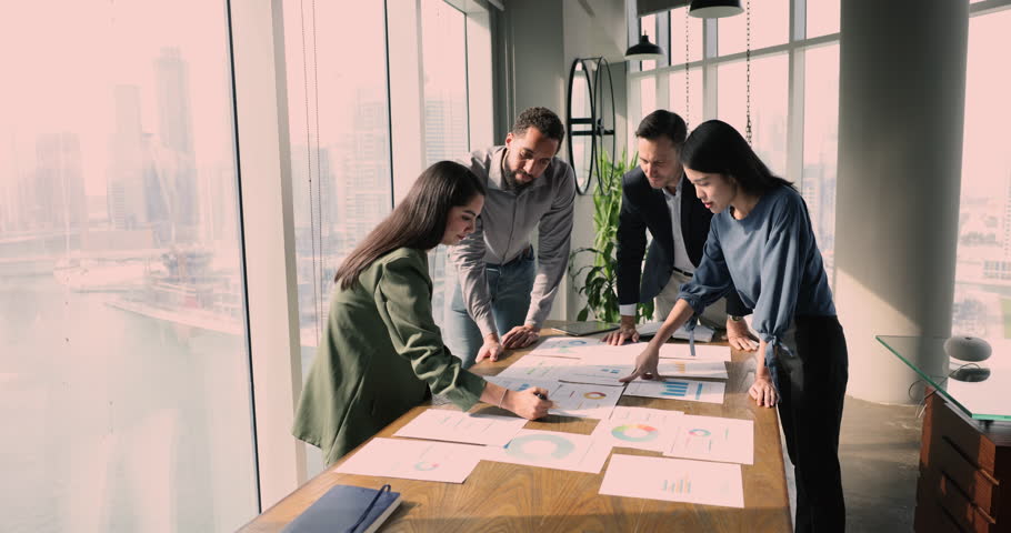 Group of business partners, stakeholders make market research, share opinion and vision, review infographic with charts and diagrams engaged in brainstorm at briefing event in company conference room