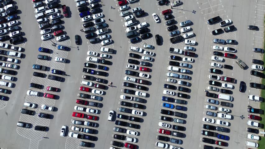 Few parking spots available and busy cars driving around looking for space in large outdoor lot in Arlington, Texas, people walking, modern parking management pavement marking number, flyover. USA