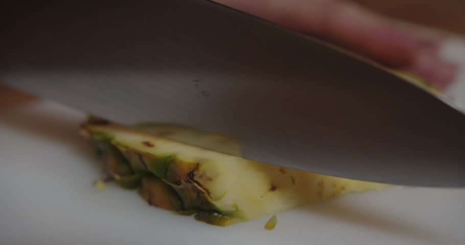 Beautiful shot of a young female bartender cutting the peel of a piece of pineapple with a knife to prepare a piña colada cocktail.