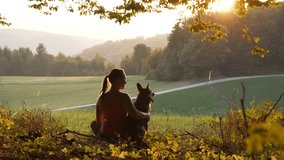 SILHOUETTE, LENS FLARE: Young lady and her dog share a peaceful moment watching sunset. Genuine moment of friendship between a dog owner and her pet in the midst of a peaceful natural environment. - Powered by Shutterstock - Get 15% off with code: PIKWIZARD15