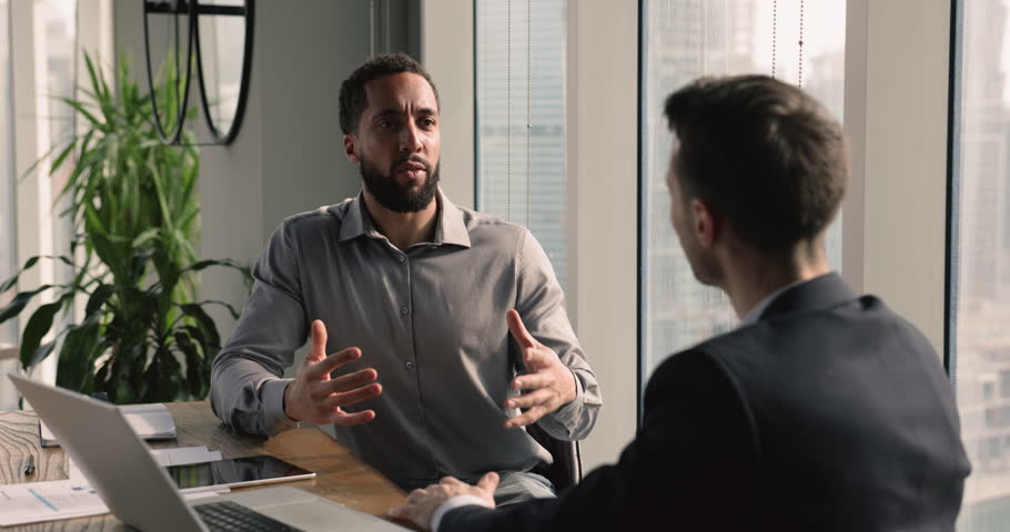 The multiethnic businessmen engaged in discussion met in office boardroom. African boss make speech, tell about upcoming project, express opinion to overcome potential challenge. Teamwork, negotiation