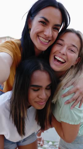 Vertical shot of three multiracial young tourist women taking video selfie portrait during summer vacation. Female friendship and travel concept.