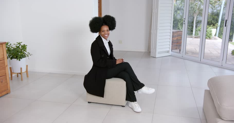 High speed photography for dynamic scenes, sitting on ottoman, woman in black coat smiling in modern living room. people, movement, full body, sitting