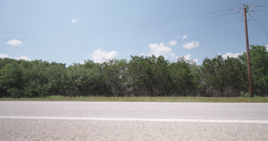 A red SUV drives past on a sunny highway in the Texas Hill Country- slider right to left
