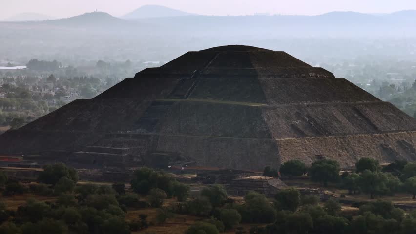Close-up drone aerial view of the Pyramid of the Sun at dawn, surrounded by mist and lush green trees. Teotihuacan, Mexico