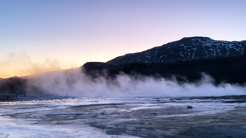A powerful geyser shoots steam into the sky against a backdrop of rugged terrain in Iceland on a sunny day. Geyser erupts in Iceland