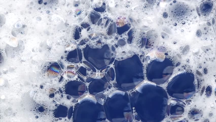 Foam background. Liquid soap bubbles, Froth bubbles rotating backdrop. Soap foam structure over blue. Soap sud macro, close-up. Clean, cleaning, washing, laundry. Top view. 