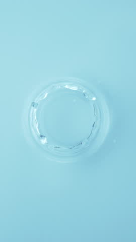 Natural water splashing. Rings and ripple top view. Drop of cosmetic essence serum falling in slow motion from above. Body moisturizing cosmetics. Beauty luxury product blue liquid vertical footage