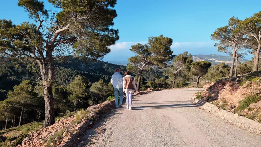 A couple of tourists are walking through the Serres de Pándols-Cavalls Protected Natural Area towards the Ermita del Pinell de Brai church. Slow motion. Tarragona, Catalonia, Spain.
