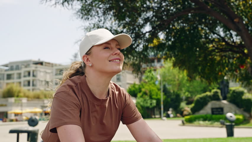 Woman rides bike on Buyukada Island, enjoys scenic views. Tourist explores urban landscape, sunny day adventure. Casual ivory cap, brown top, sightseeing cyclist captures local culture.