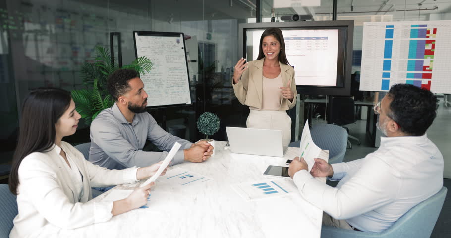 Woman leading business presentation or meeting in boardroom, speaking to three colleagues, engaged in discussion about project progress, financial reports, or strategic planning. Negotiations, seminar