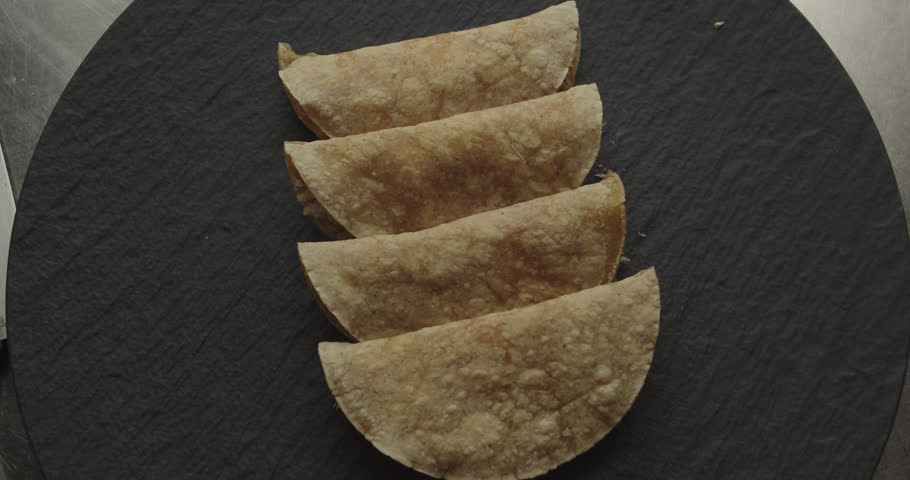 Beautiful slow motion shot of the presentation of a plate of 4 tacos or Mexican tortillas dimly lit with white light in an industrial kitchen of a Mexican restaurant.