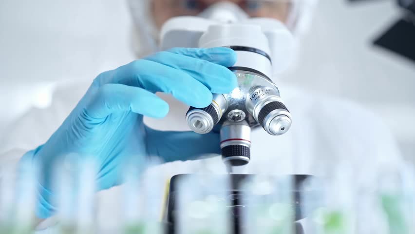 Professional scientist in protective gear is using microscope in a laboratory setting, close-up. Science and medicine concepts