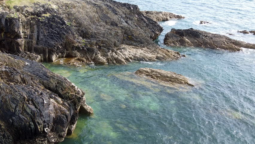 Rocky Shoreline at Low Tide With Clear Water and Marine Life in Coastal Area. Clear waters revealing marine life near rocky shoreline during low tide, showcasing the natural beauty of the coast.